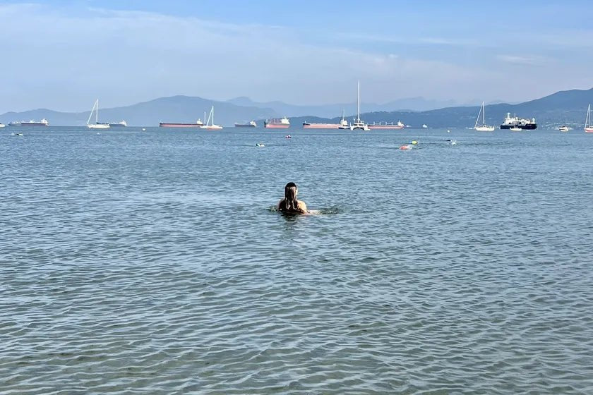 A swimmer resting in calm open water, sailboats and mountains along the horizon