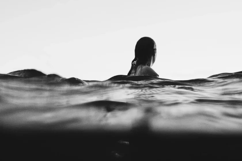 Black-and-white photograph of a swimmer with wet hair, low in open water under a pale sky