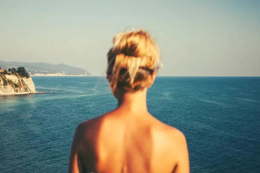 A figure facing open ocean under a pale sky — the lived-in coast where sea spray comes from.