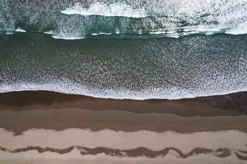 An aerial view of the tide meeting the shore in bands of sea, foam and wet sand