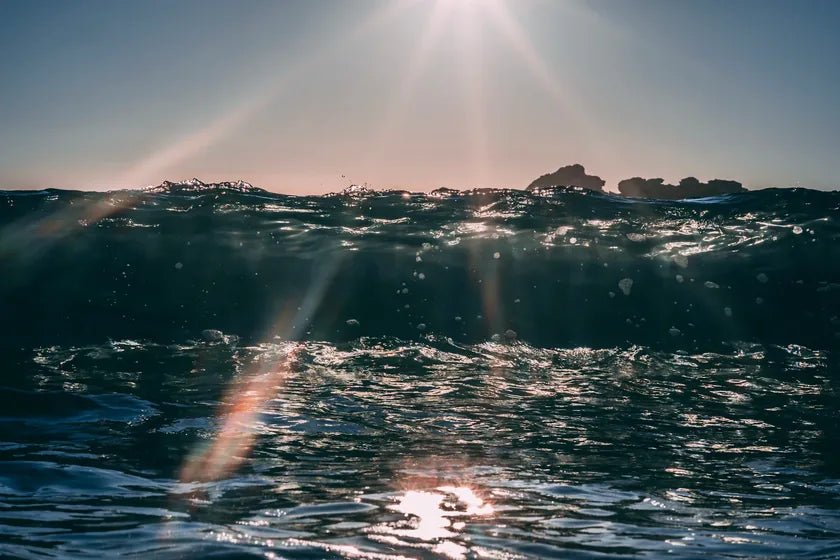 Sunlight breaking over a choppy dark sea, with rocks on the horizon