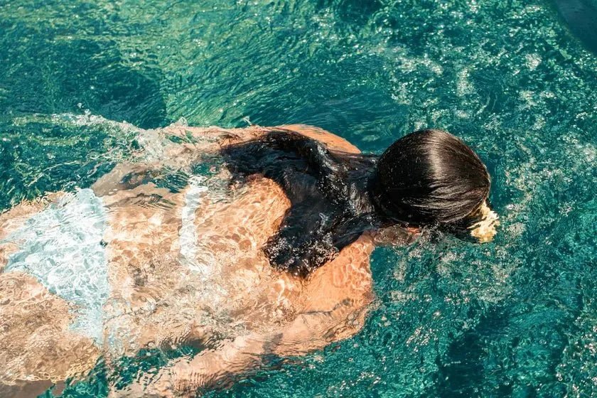 A swimmer with dark hair moving through clear turquoise water in summer light